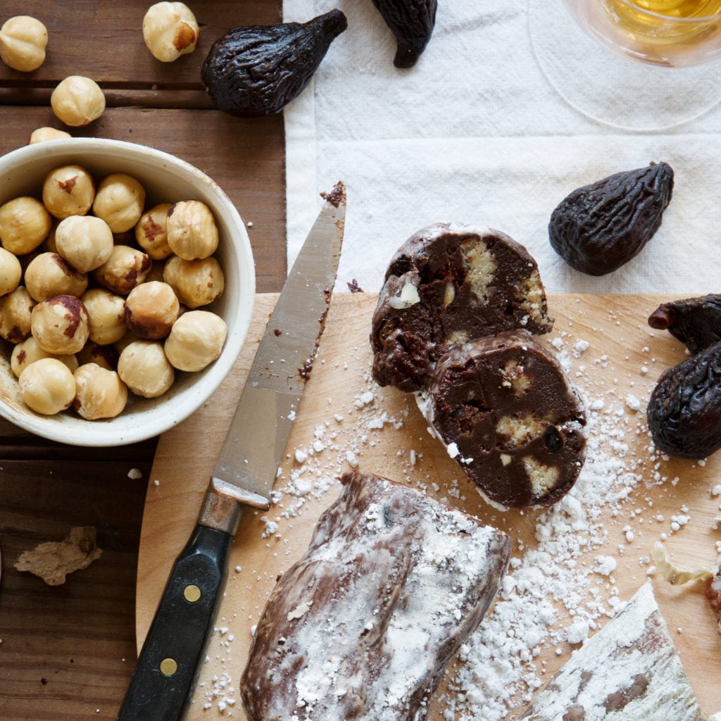 Sliced chocolate salami with a bowl of hazelnuts and figs