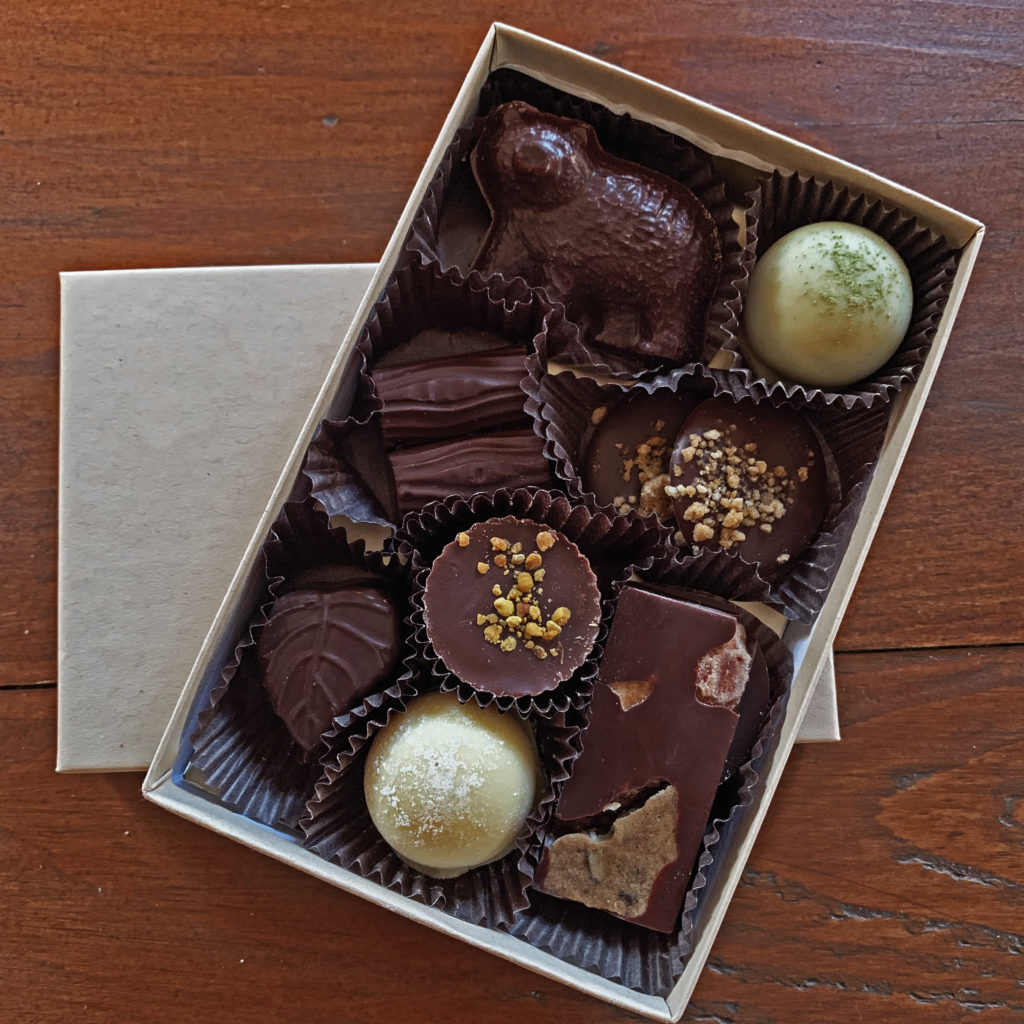 Assorted chocolate bonbons in the shape of bears, logs, leaves, rocks and other shapes in a kraft box on a wood background