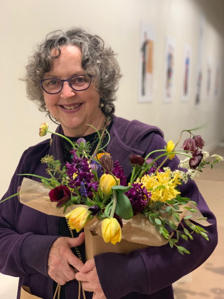 Older woman holding bouquets of purple and yellow flowers