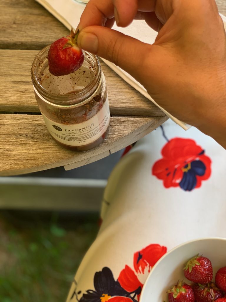Hand holding a strawberry being dipped in Tavernier chocolate