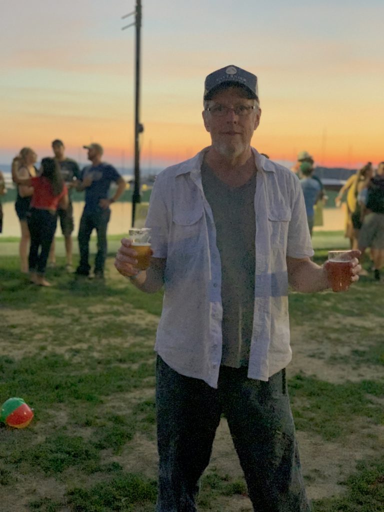 John Singer holding two glasses of beer at sunset at the VT Brewers Festival