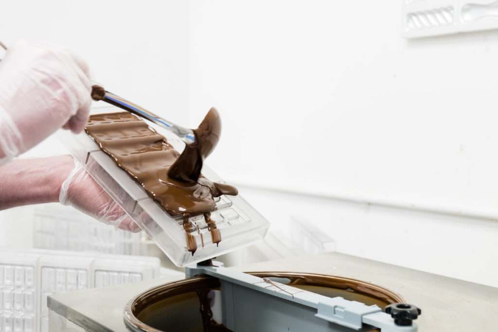 Gloved hands pouring melted chocolate into a chocolate mold