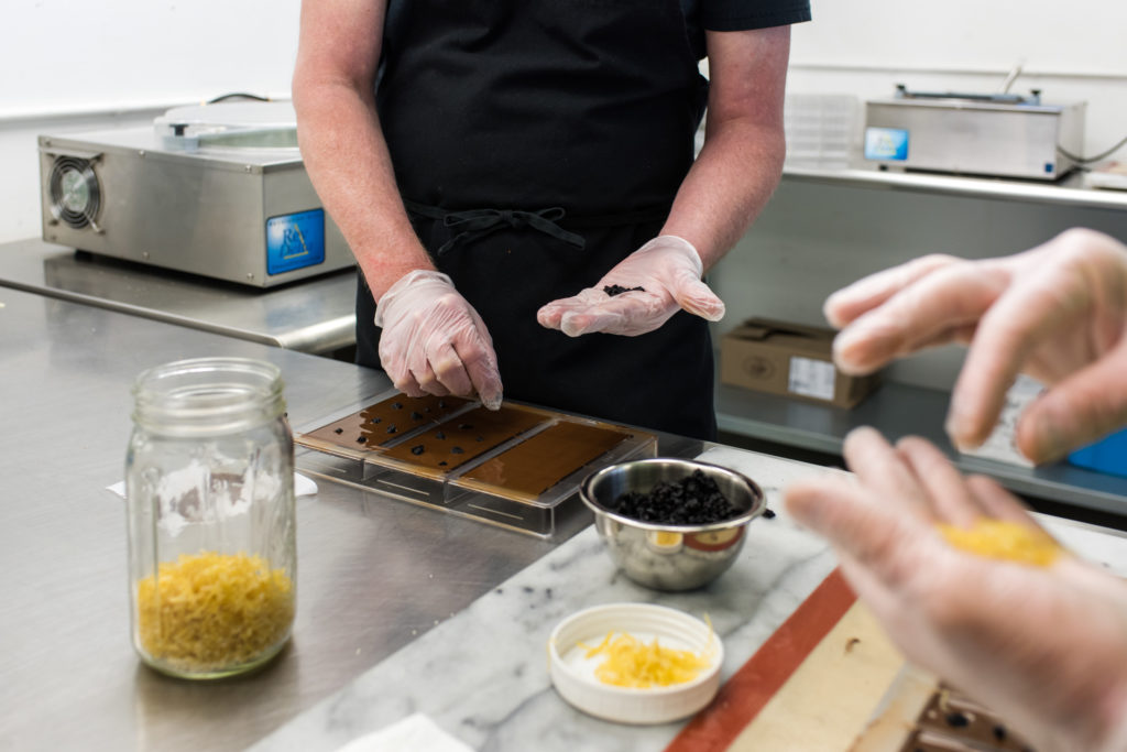 Gloved hands pressing ingredients into the chocolate bars