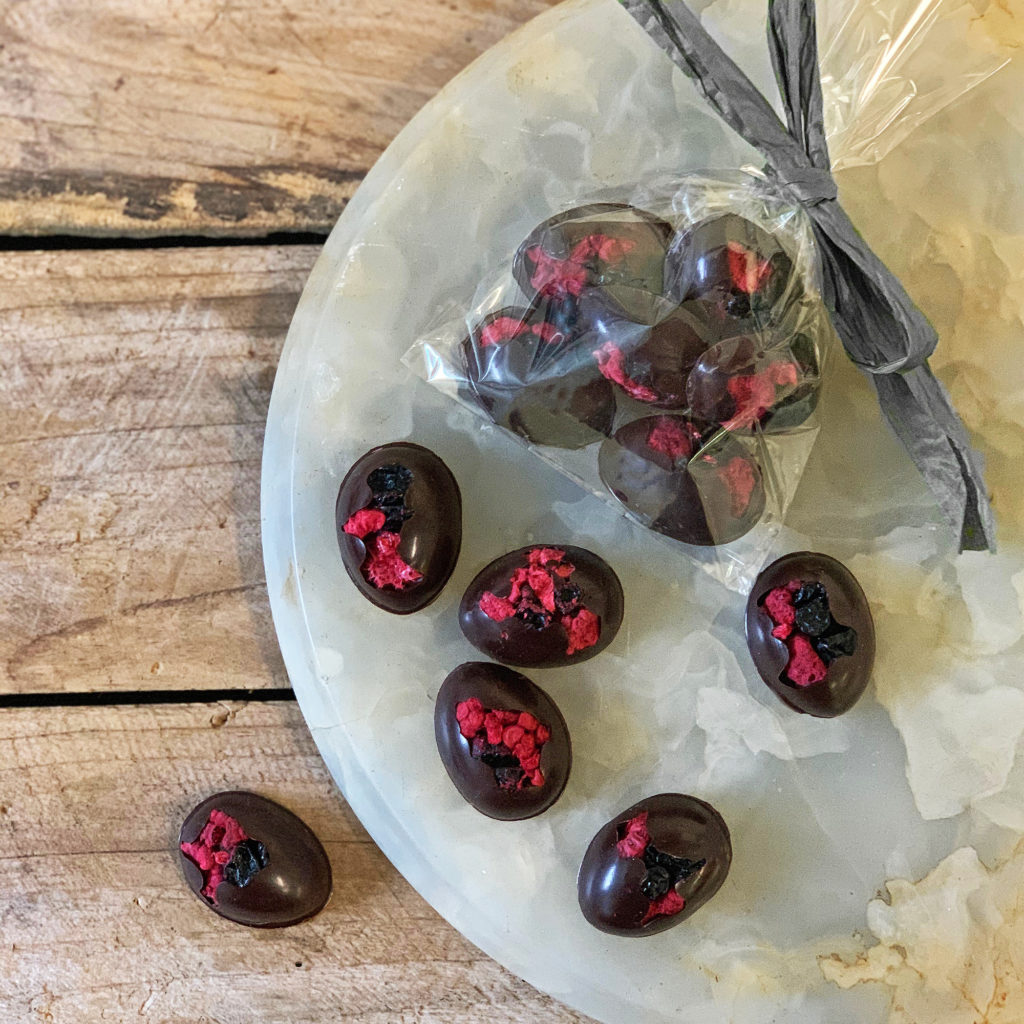 Fruit eggs with raspberry and blueberries. Several of the eggs are sitting on a marble plate. Others are in a clear plastic bag tied with a silver bow