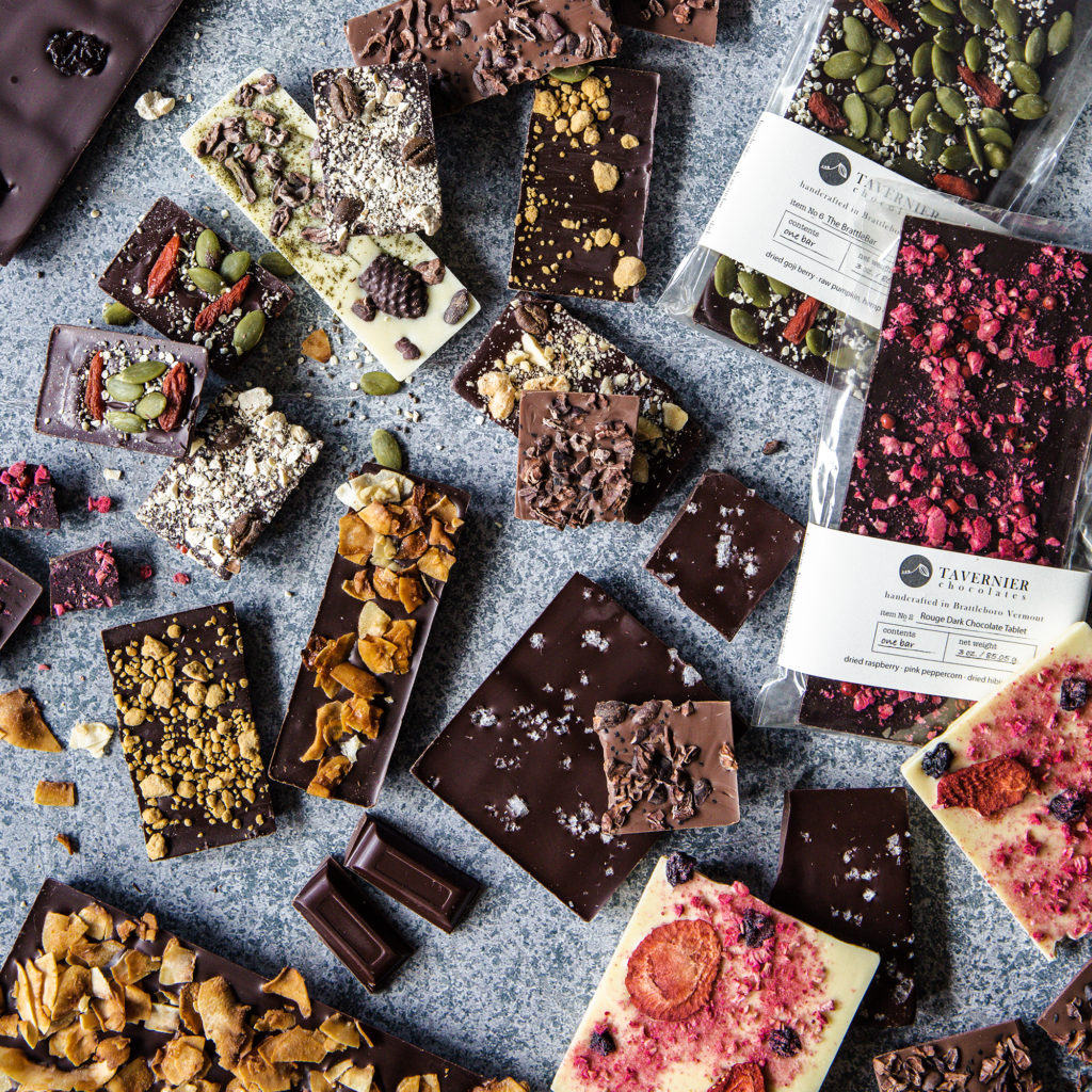 large chocolate tablets and small chocolate bars decorated with fruits nuts coconut and seeds in a jumbled array on a stone background