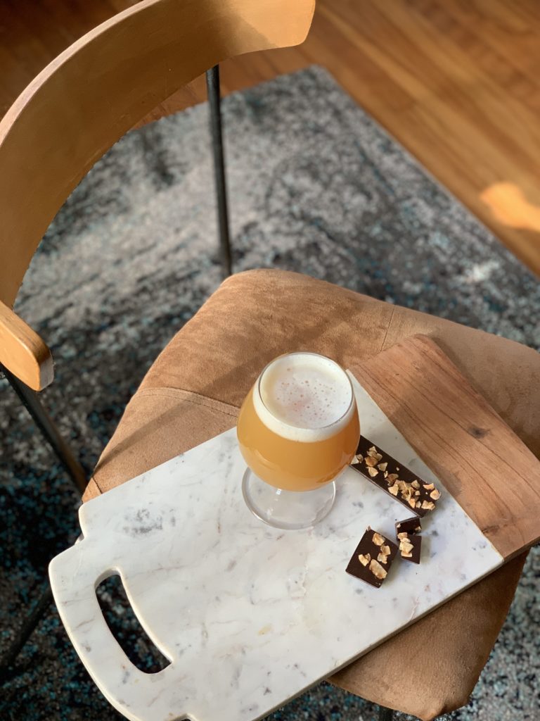 Overhead shot of a craft beer and hazelnut chocolates sitting atop a marble cheese board.