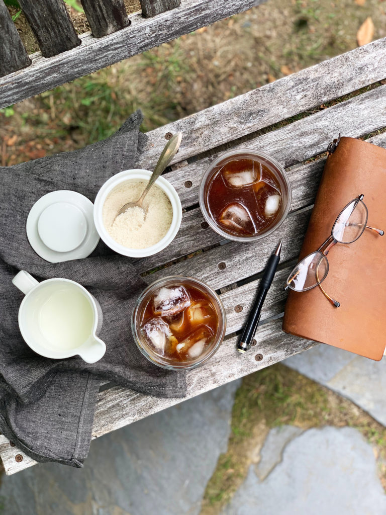 Overhead shot of iced cold brewed cacao coffee and creamer. The coffee is sitting on a wooden bench