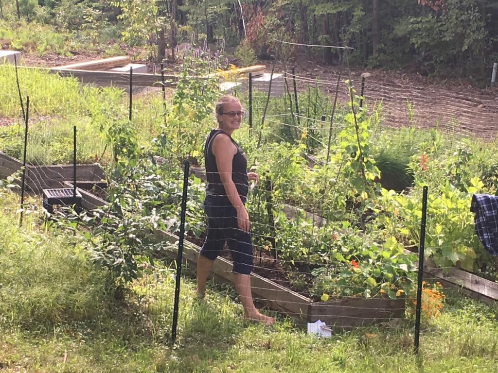 Woman stands in a large garden behind a wire fence