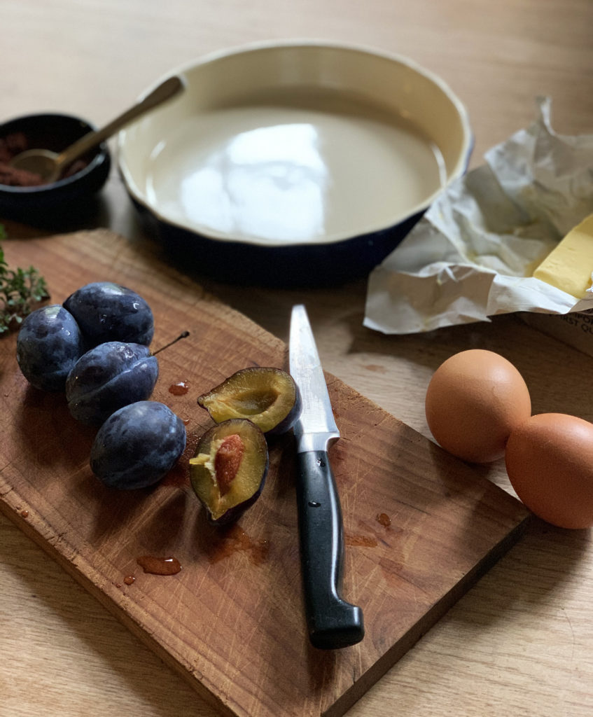 Wooden cheese board topped with figs and thyme. Next to the board are two eggs and a package of butter