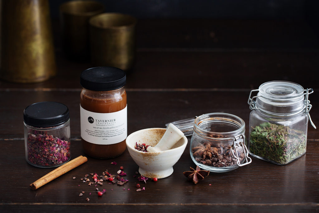 Small glass jars featuring spices like mint, star anise, and rose petals.