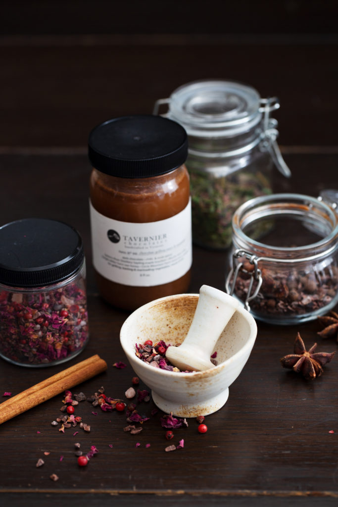 Small glass jars featuring spices like mint, star anise, and rose petals.