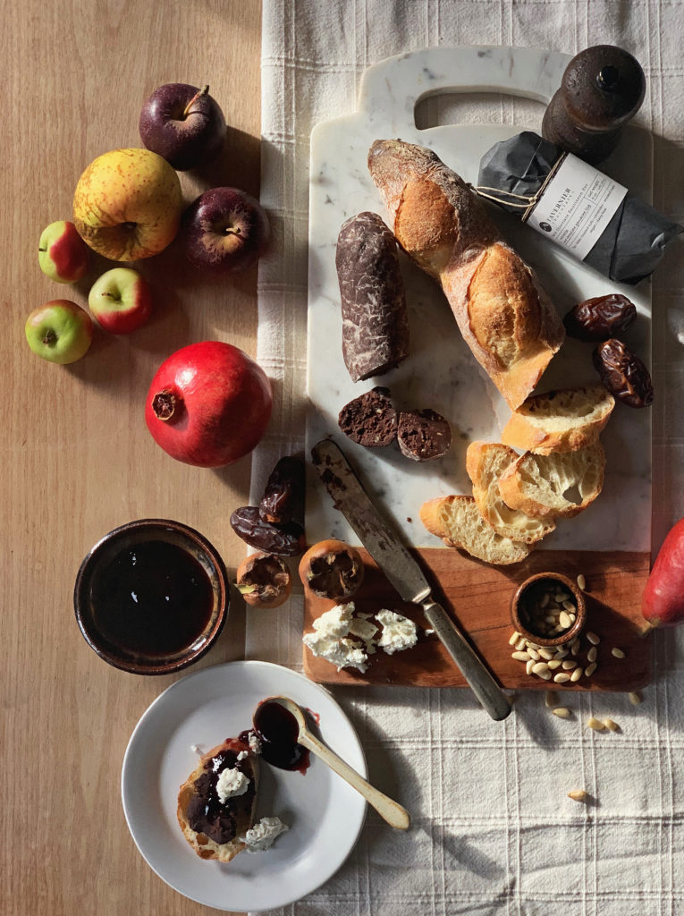 Overhead shot of a cheese board with bread, figs, pine nuts, and Tavernier chocolate charcuterie.