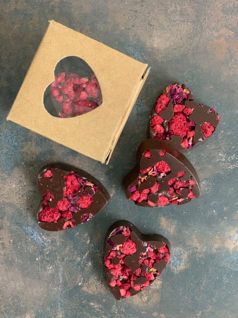 four dark heart shaped chocolates and a little kraft heart window box on a rustic weathered grey background