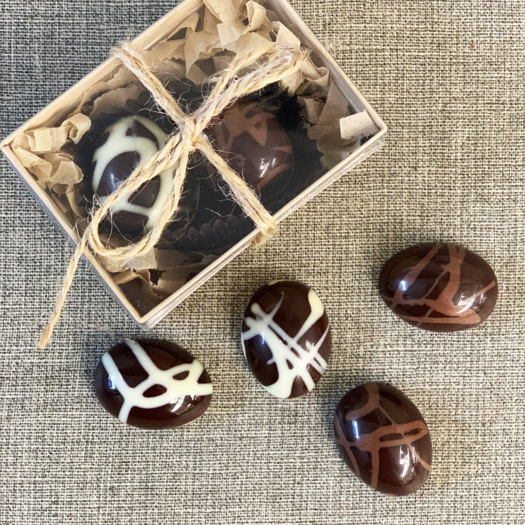 tiny chocolate easter eggs decorated with white chocolate and milk chocolate swirls on a burlap background, and a box with a clear top with eggs inside tied with rustic burlap twine