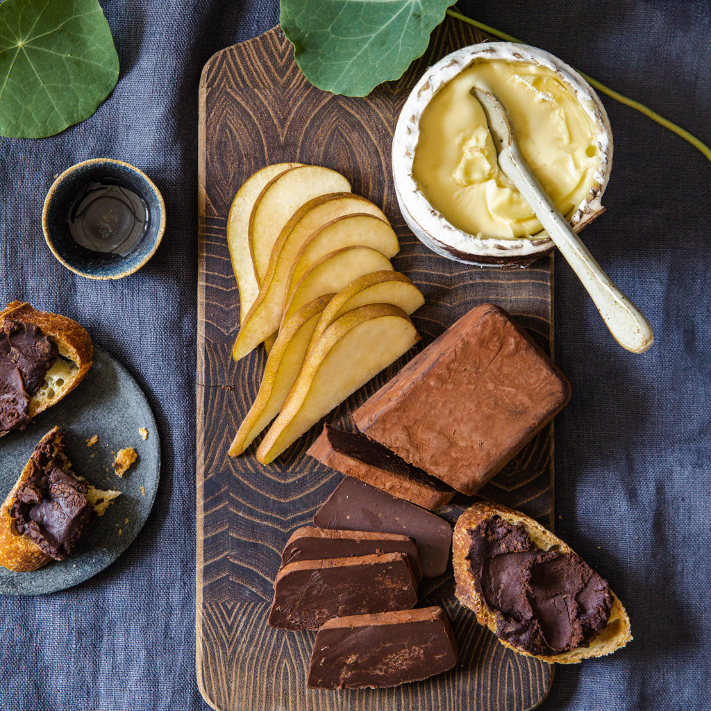 Pate chocolat on a wood board with sliced pears and soft rind cheese on dark blue fabric with nasturtium leaves