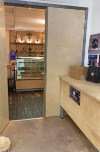 Door open into a small industrial looking shop with a chocolate candy case, warm lighting and worn wooden floors