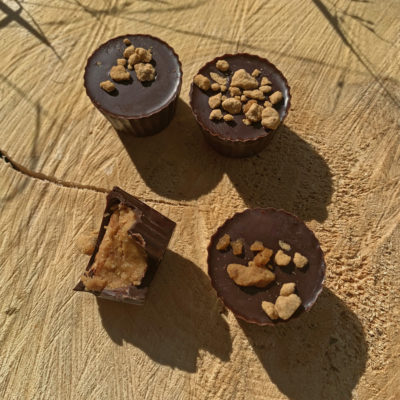 four chocolate peanut butter cups, one with a bite taken out of it, sprinkled with maple sugar nuggets, sitting on a tree stump in the sunlight.