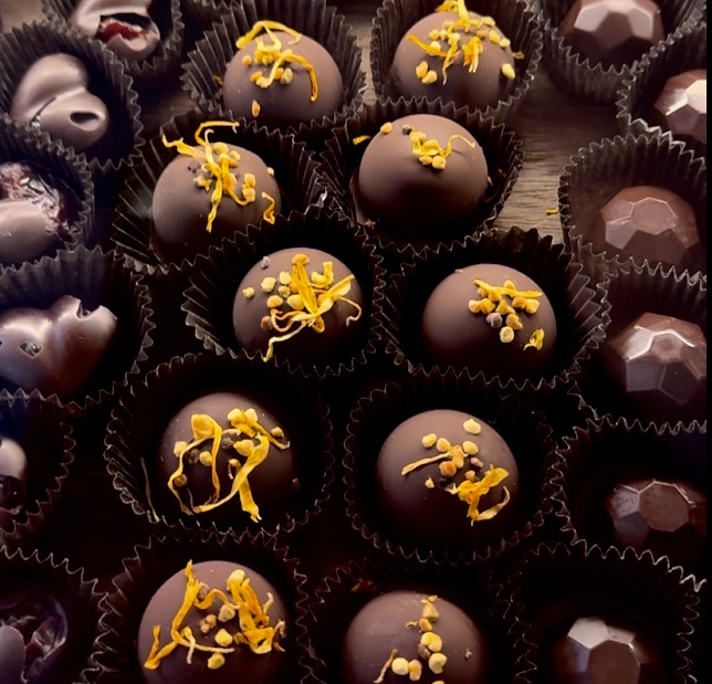 dark chocolate truffles in a case decorated with bee pollen and yellow calendula blossoms